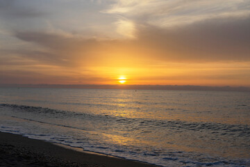 At sunrise, the ocean is tranquil, the sky a vibrant orange, and the sun peeks through the clouds