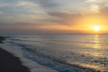 At sunrise, the ocean is tranquil, the sky a vibrant orange, and the sun peeks through the clouds