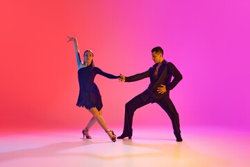 Young man and woman, ballroom dancers dancing expressively energetic Rumba in neon lighting against vibrant gradient background. Concept of dance and music, sport, action, competition, classical. Ad