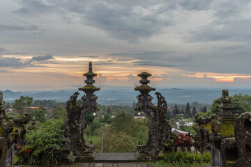 Fototapeta premium Gate with lamps and greenery with a sunset sky and buildings in the background