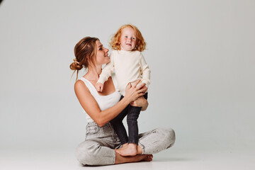 Mother and daughter sit on floor in front of white background, family time together, home lifestyle...