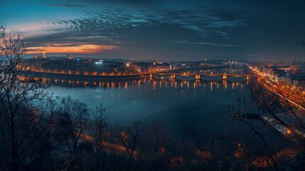 Fototapeta premium A panoramic night shot of a bridge spanning a river, with the illuminated cityscape in the background.