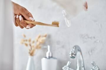 African American woman in bathrobe holding toothbrush in modern bathroom, emphasizing beauty and hygiene routine.