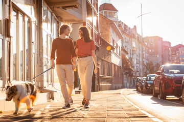 Happy married couple is walking around city with their Aussie dog. Sunset light in background....