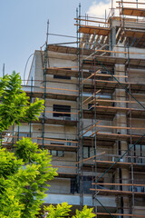A multi story building under construction stands against a blue sky. The intricate scaffold...