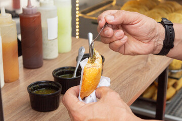 A man applying a spoonful of hot sauce to an egg-stuffed Arepa (Arepa de huevo con aji). Delicious fried arepa of Colombian origin.