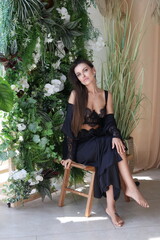 A beautiful woman in black lingerie and a bathrobe is sitting in the pool in a hotel room. A brunette girl is sitting on a chair, behind a plant. Portrait of a lady with big lips and long hair