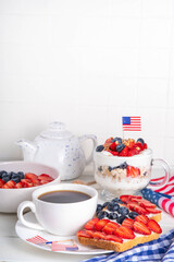 USA patriotic breakfast or brunch with american flag decorated oatmeal, layered yogurt granola dessert, toast sandwiches with fresh berries, and coffee cup on kitchen garden table