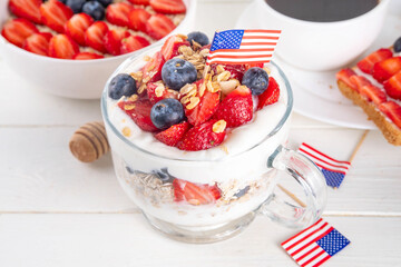 USA patriotic breakfast or brunch simple recipe idea, layered granola dessert, or overnight oatmeal in glass decorated with white whipped yogurt, blue and red berries and american flag