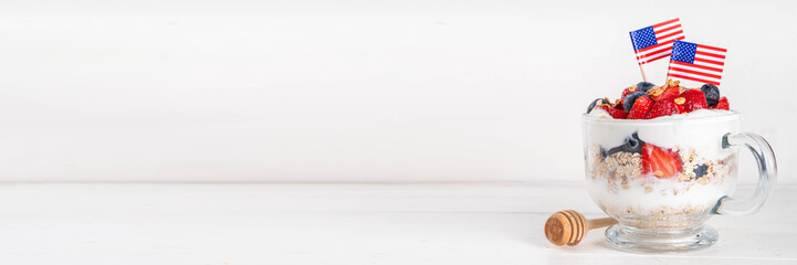 USA patriotic breakfast or brunch simple recipe idea, layered granola dessert, or overnight oatmeal in glass decorated with white whipped yogurt, blue and red berries and american flag