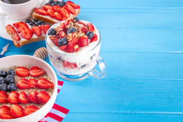 USA patriotic breakfast or brunch with american flag decorated oatmeal, layered yogurt granola dessert, toast sandwiches with fresh berries, and coffee cup on kitchen garden table