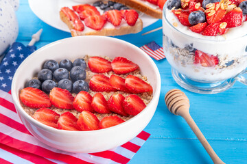 USA patriotic breakfast or brunch with american flag decorated oatmeal, layered yogurt granola dessert, toast sandwiches with fresh berries, and coffee cup on kitchen garden table