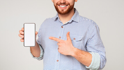 Cropped of smiling man holding latest slim cellphone with white empty screen and pointing at it,...