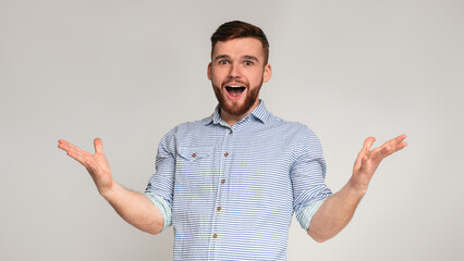 Fototapeta premium Hey you. Young exited bearded man raising hands and happy screaming on grey studio background, panorama
