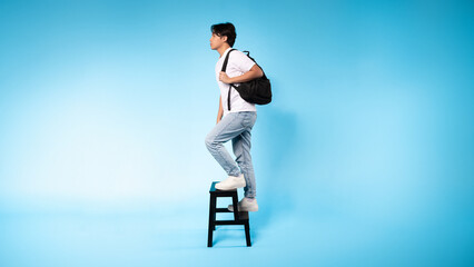 Asian guy is standing on a stool while wearing a backpack. He appears to be preparing for a task or...