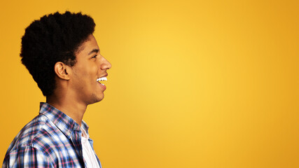 Profile portrait of smiling afro guy, looking at copy space over orange background