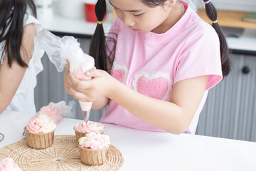 Asian little cute child girl enjoy making cupcakes with friend at home kitchen, squeezing...