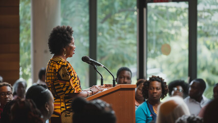 Female Speaker Engaging Audience at Indoor Community Event in Vibrant Traditional Attire