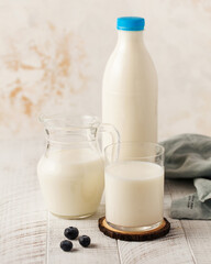 Fresh milk in a bottle with a blue cap, a jug, and a glass on a wooden coaster