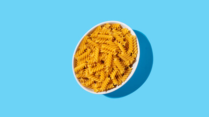 Uncooked fusilli pasta spirals in a white bowl on a blue background