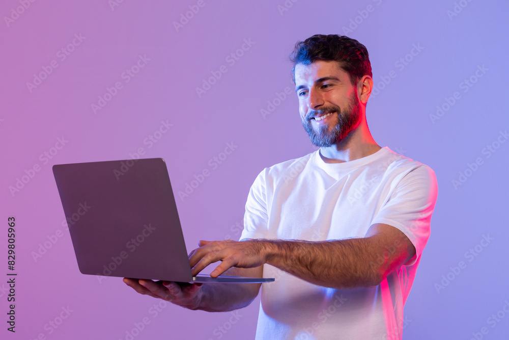 Poster A man in a white shirt is standing and holding a laptop in his hands. He appears focused on the screen, possibly working or studying. The background is simple and devoid of any distracting elements.