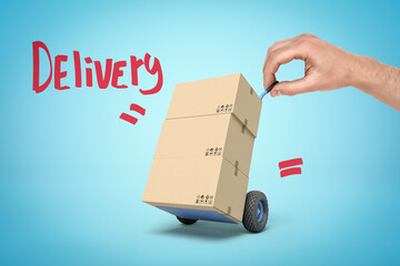 Hand holding tiny hand truck with cardboard boxes and 'Delivery' sign on blue background