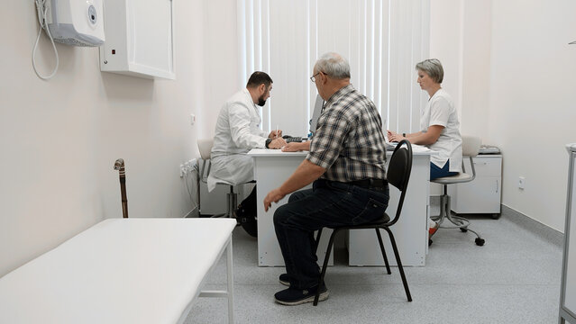 Senior man patient sitting on chair by the table of a doctor and a nurse. Clip. Medical checkup visit at the hospital.