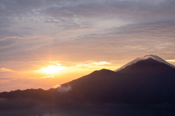 Sunrise over Mount Batur with a golden sky and silhouetted mountains. Travel