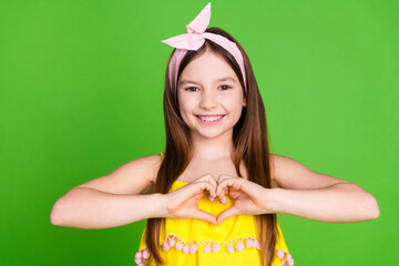 Photo of girlish pretty little lady dressed yellow outfit smiling showing arms heart isolated green...