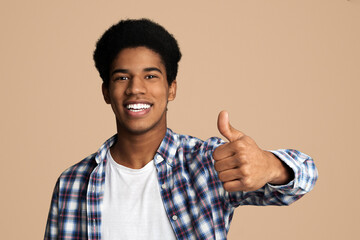 Overjoyed african guy showing thumb up and widely smiling, white studio background