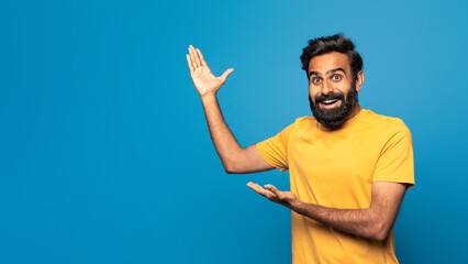 A cheerful Indian man wearing a yellow shirt smiles widely while enthusiastically gesturing with...