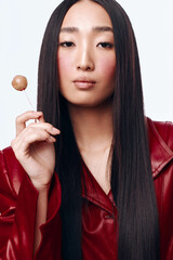 Stylish woman with long black hair wearing a red leather jacket holding a lollipop in hand