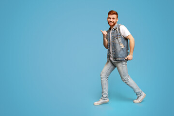 Naklejka premium Cool millennial man dancing with thumbs up gestures on blue background, studio, copy space, full length