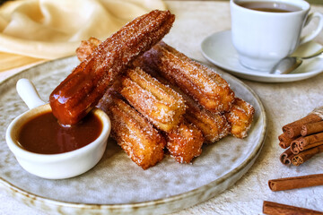 Churros. Churros with hot chocolate sauce, sugar and cinnamon.  Churros on a plate with hot chocolate sauce. A traditional Spanish dessert. Street fast food.