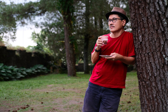 Man holding a cup of hot chocolate while leaning on a tree in the park