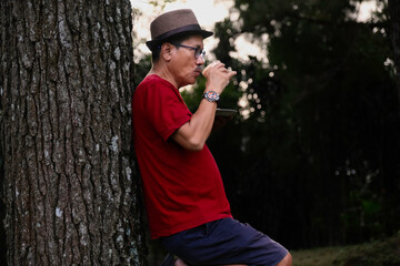 Man sipping a cup of hot coffee while leaning on a tree in the park