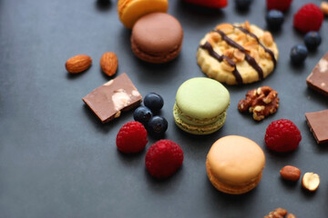 Macarons, chocolate, cookies, berries and various nuts on dark blue background. Selective focus.