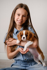 Happy girl holds cute Cavalier King Charles Spaniel puppy in her arms, gently hugs him to her,...