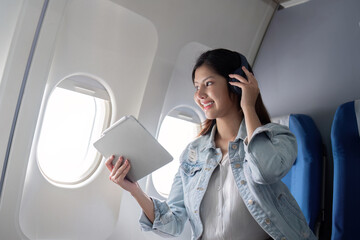 Asian woman using tablet and headphones on airplane during flight