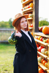 Portrait of young girl with red hair in autumn black cardigan posing with pumpkins on a farm. Copy...