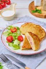Potato pancakes stuffed with minced meat on a ceramic plate on a light wooden background. Served with fresh cucumber and cherry tomatoes. Belarusian cuisine.