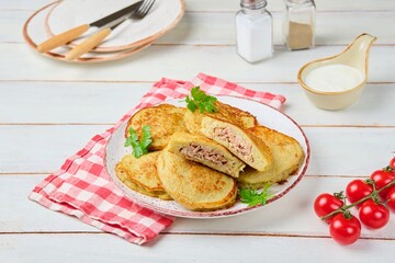 Potato pancakes stuffed with minced meat on a ceramic plate on a light wooden background. Served with sour cream. Belarusian cuisine.
