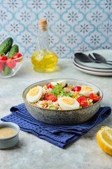 French rice salad with canned tuna, cherry tomatoes, corn and cucumber in a ceramic bowl on a gray concrete background. Summer Picnic salad.
