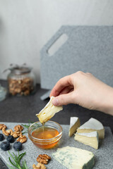 woman hand holding piece of cheese and honey dripping from it. Cheese plate on kitchen counter