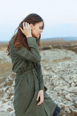 Mystery woman in olive green trench coat gazing at rocky horizon from hilltop