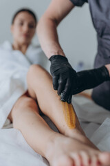 Naklejka premium Beautician depilating young woman's legs with liquid sugar in spa center