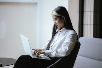 Modern Asian businesswoman sitting and working using a laptop Smart phone in office work