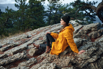 A woman enjoying the beauty of nature while sitting on top of a mountain in a yellow raincoat and...