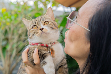 Shot of mature Asian woman playing with her cute cat while relaxing in the garden at home.