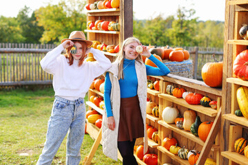 Portrait of two beautiful smiling girls holding pumpkin in front of pumpkin rows on farm during the...